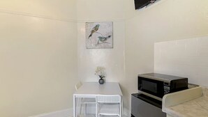 A small kitchenette with a microwave, a white table with two chairs, and a painting of birds on the wall. - Pads on Pasadena Ave (Los Angeles)