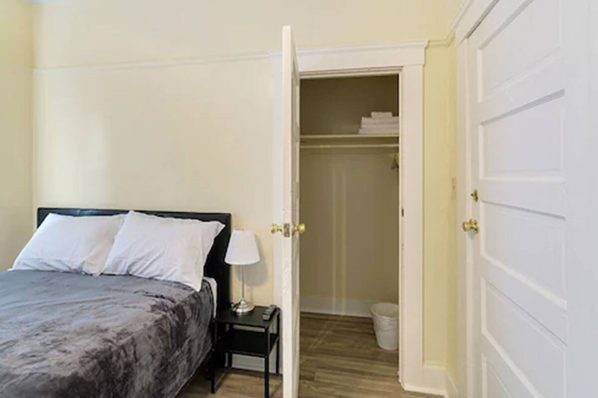 Ein Schlafzimmer mit Bett, Nachttisch, Lampe und offenem Kleiderschrank.
