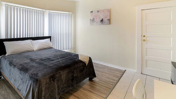 A bedroom with a bed, a door, and a window with blinds. - Pads on Pasadena Ave (Los Angeles)