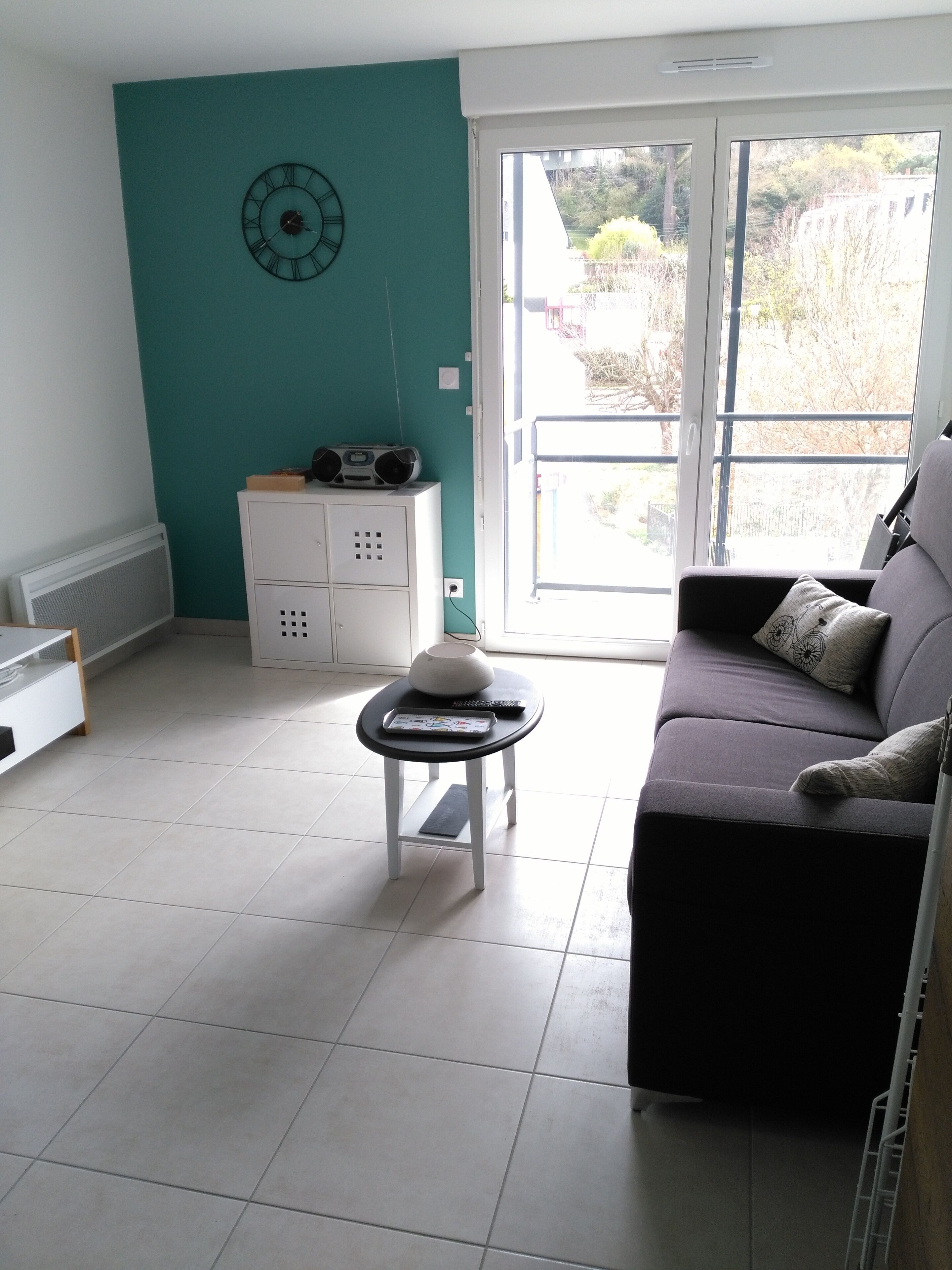 Un salon avec un mur de couleur turquoise, un meuble blanc, un canapé et une petite table sur laquelle se trouvent une radio et une télécommande.