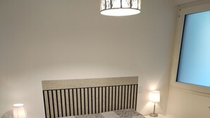 A neatly made bed with a patterned bedspread, two bedside tables with lamps, and a window with a view.