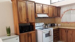 A kitchen with wooden cabinets, a white stove, and a black microwave. - Private Apartment House 2 Bedroom 5 mins SJO Airport Furnished Spacious Kitchen (Alajuela)