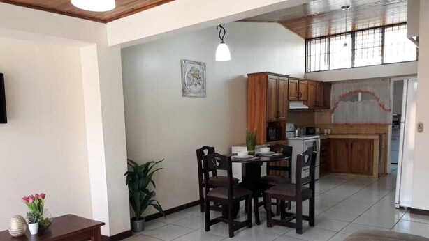 A spacious living area with a dining table and chairs, a sofa, and a kitchen in the background. - Private Apartment House 2 Bedroom 5 mins SJO Airport Furnished Spacious Kitchen (Alajuela)