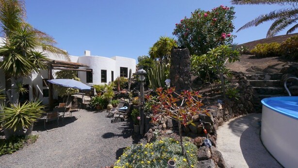 Un jardin avec une piscine, un espace salon extérieur et un bâtiment blanc.