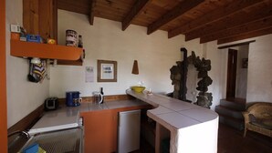 Une cuisine compacte équipée d’un réfrigérateur, d’une machine à café et d’un grille-pain. On y trouve une étagère en bois au-dessus du plan de travail et un élément décoratif en pierre sur le mur.