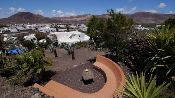 A courtyard with a stone bench, surrounded by plants and a view of a town with white buildings and mountains in the background. - CASA CALDERETA, country house in unique nature. (Guatiza)