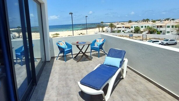 A balcony with a sun lounger, two chairs, and a table with a drink. - Casa Iris El Cotillo Fuerteventura Adults Only (El Cotillo)