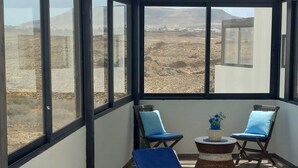 A sunroom with two lounge chairs and a small table, large windows offering a view of a barren landscape. - Casa Iris El Cotillo Fuerteventura Adults Only (El Cotillo)