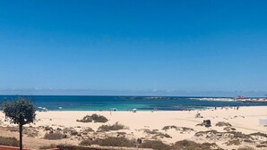 A beach with clear blue water, sandy shore, and sparse vegetation. - Casa Iris El Cotillo Fuerteventura Adults Only (El Cotillo)