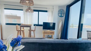 A bedroom with a large bed, a TV, a small table with chairs, and a view of the beach through the window. - Casa Iris El Cotillo Fuerteventura Adults Only (El Cotillo)