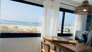 A room with a wooden dining table, a chair, and a view of the beach and ocean through large windows. - Casa Iris El Cotillo Fuerteventura Adults Only (El Cotillo)