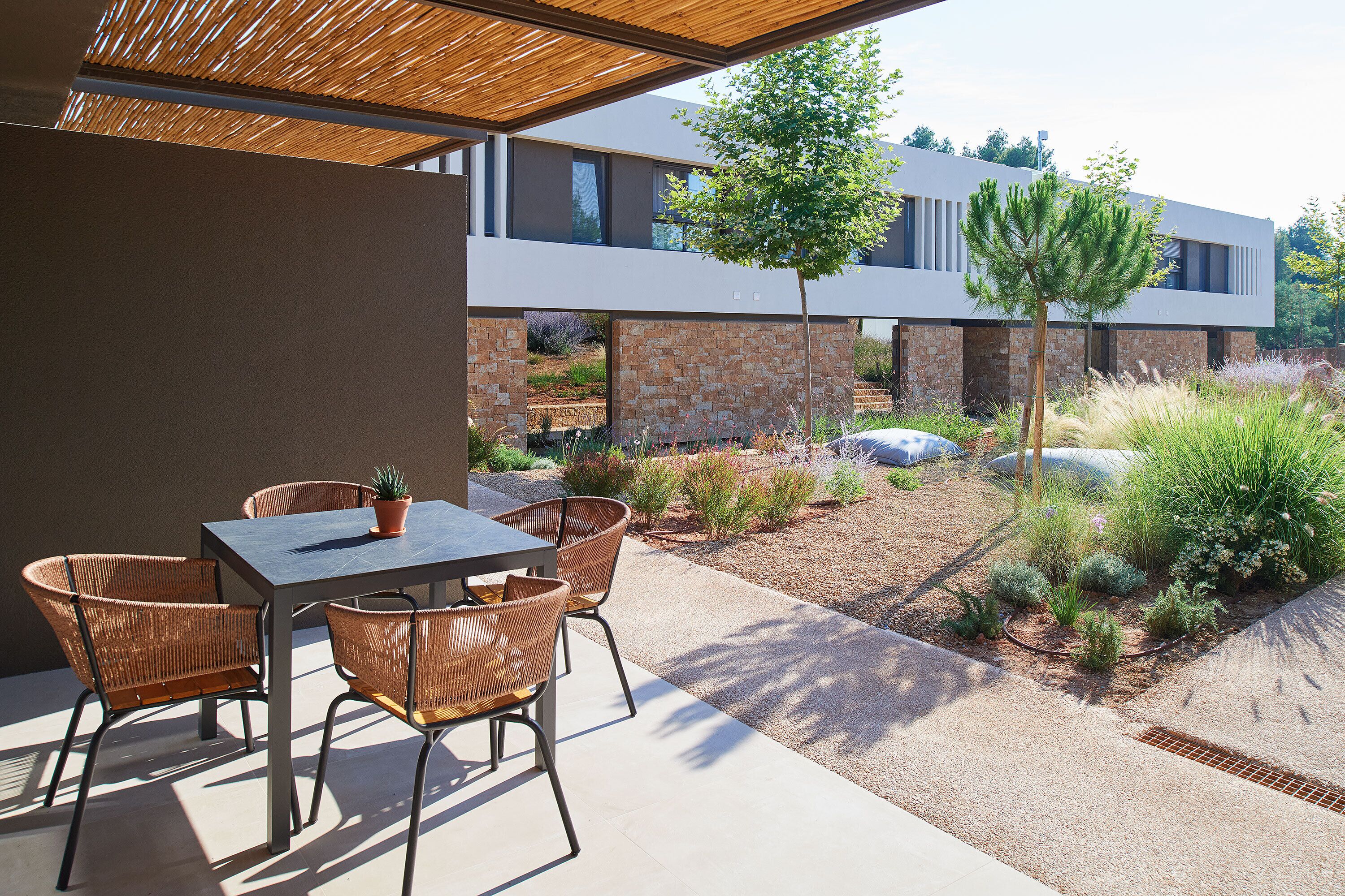 An outdoor patio with a table and chairs, a potted plant, and a modern building in the background.