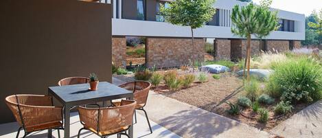 An outdoor patio with a table and chairs, a potted plant, and a modern building in the background.