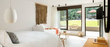 Een moderne hotelkamer met een groot bed, een bureau met een laptop, een televisie en uitzicht op een buitenplaats.