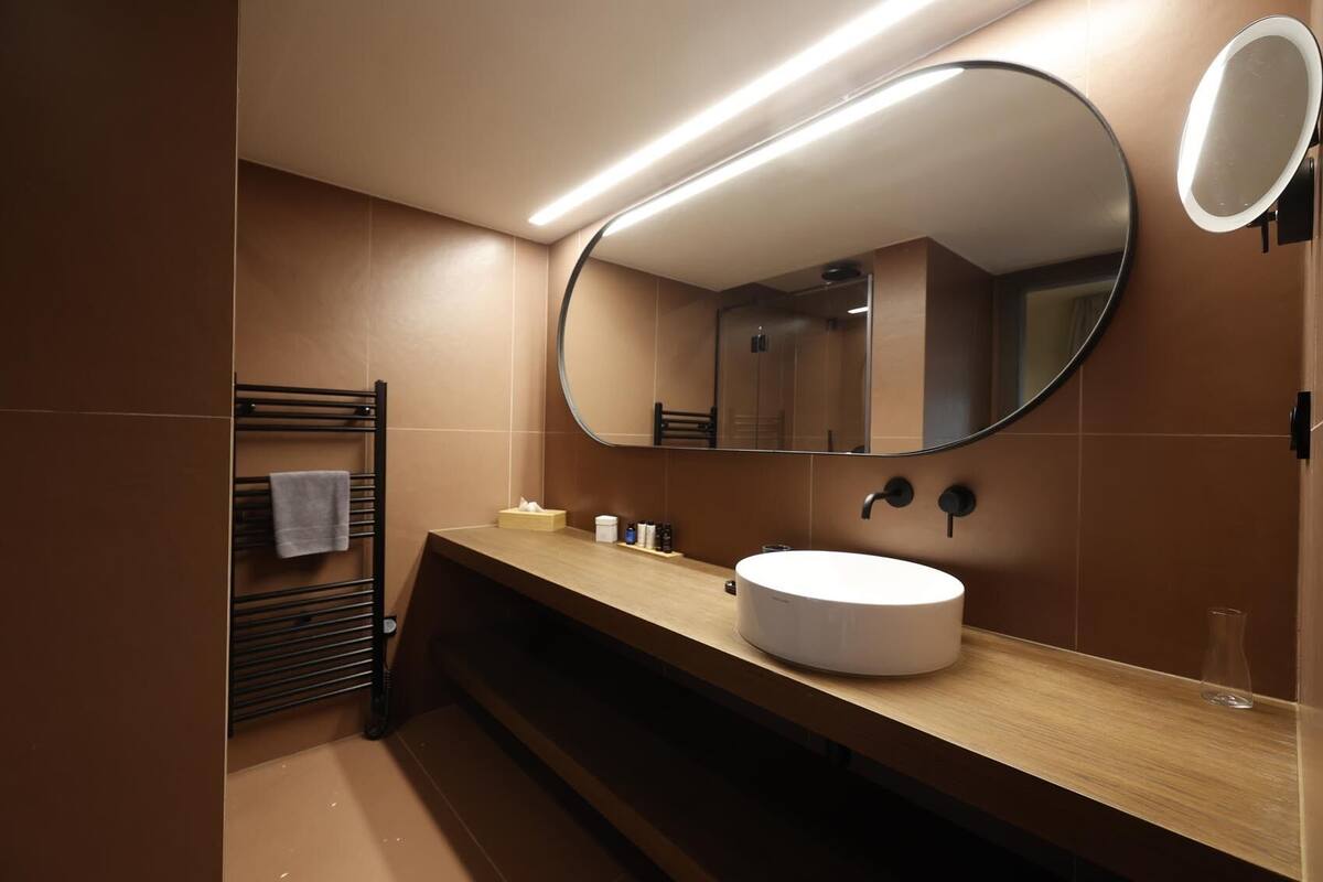 Un baño moderno con un espejo redondo, un tocador de madera y un perchero para toallas.