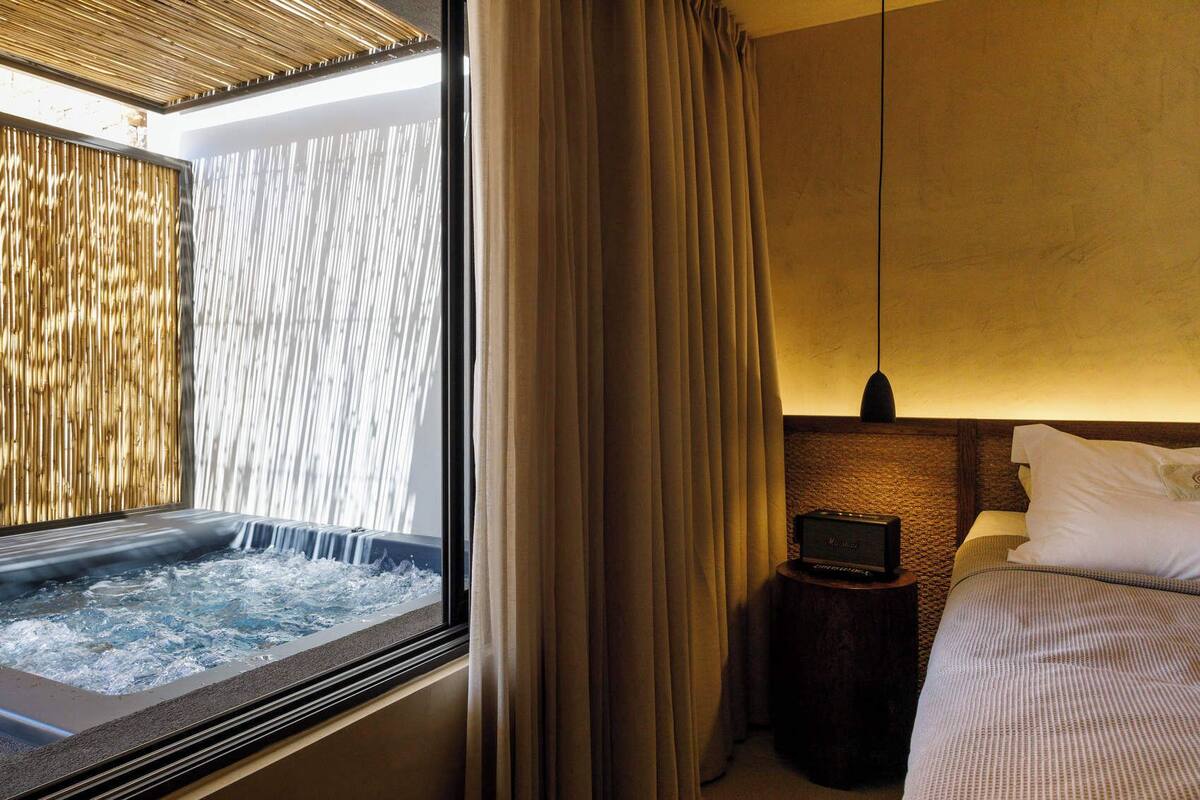 Habitación de hotel con jacuzzi, cama, mesita de noche con radio y vistas a una cascada a través de una ventana.