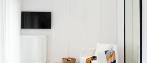 A modern, minimalist room with a white sofa, a large mirror, a television mounted on the wall, and a woven basket on the floor.
