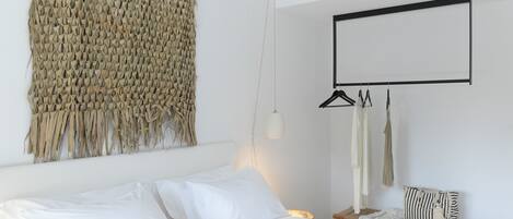 A bedroom with a bed, a hanging light, a wall-mounted mirror, and a woven textile decoration.