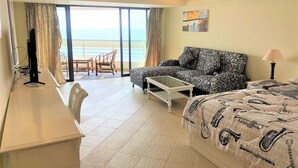 A hotel room with a balcony, a sofa, a bed, a desk, and a television. - Metro Jomtien Condotel - Sleeps 2 (Pattaya)