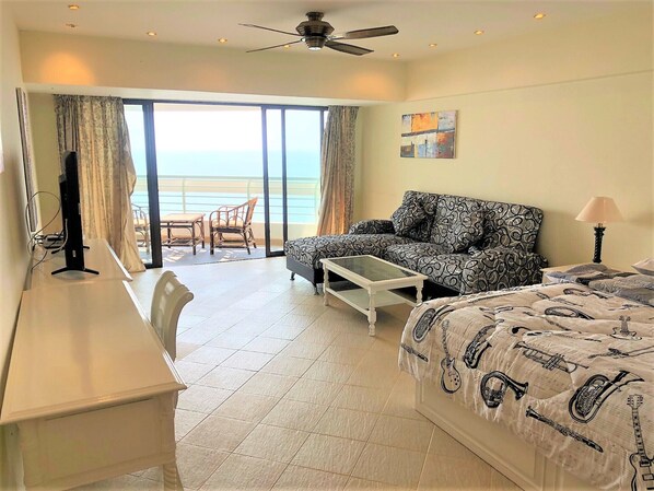 A hotel room with a balcony, a sofa, a bed, a desk, and a television.