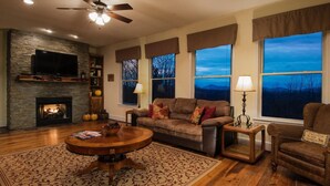 A cozy living room with a fireplace, comfortable seating, and large windows offering a view of the outdoors. - 6 BR Enormous, 4700 Square Foot Vacation Home in a Scenic Mountain Setting! (Boone)