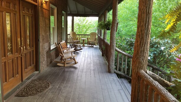 A wooden porch with rocking chairs and a table, surrounded by trees. - 6 BR Enormous, 4700 Square Foot Vacation Home in a Scenic Mountain Setting! (Boone)