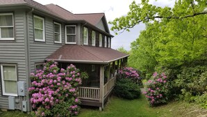A two-story house with a covered porch, surrounded by lush greenery and flowering bushes. - 6 BR Enormous, 4700 Square Foot Vacation Home in a Scenic Mountain Setting! (Boone)