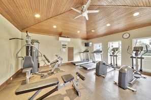 A gym with various exercise equipment, a ceiling fan, and a clock on the wall.