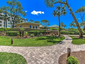 A landscaped pathway leading to a building with a green roof, surrounded by well-maintained lawns and trees.