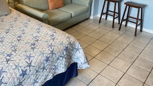 Un dormitorio con cama, sofá verde, pequeña cocina y un taburete de bar.