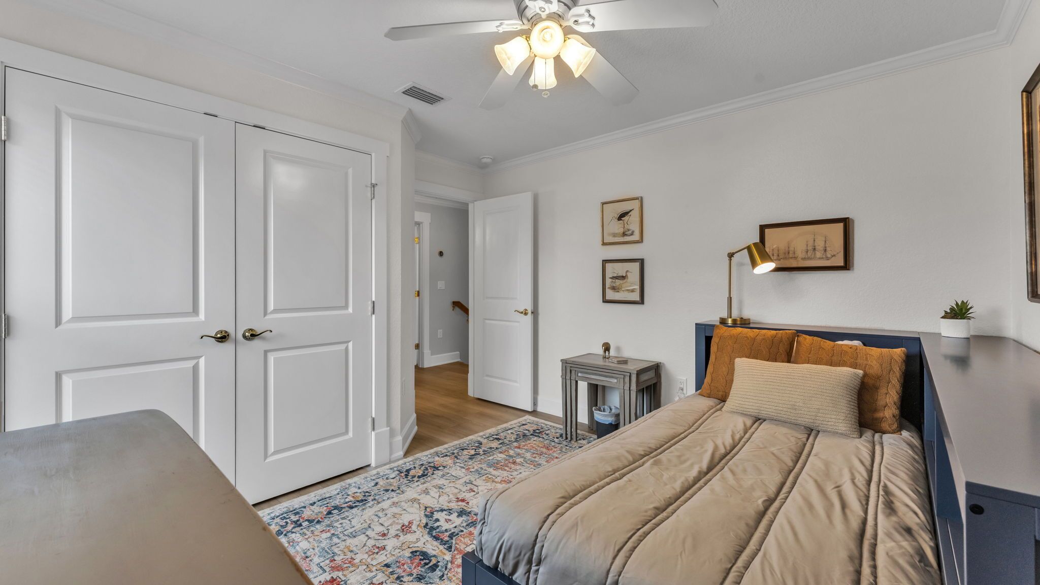 Une chambre à coucher avec un lit, un bureau, une chaise, un ventilateur de plafond et une porte.