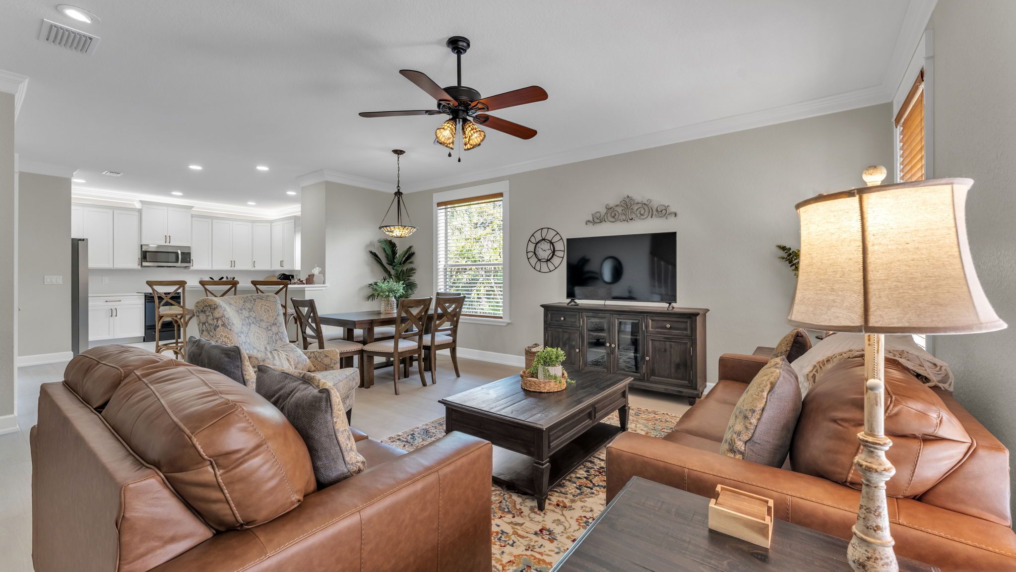 A modern living room with leather sofas, a coffee table, a TV, and a ceiling fan.