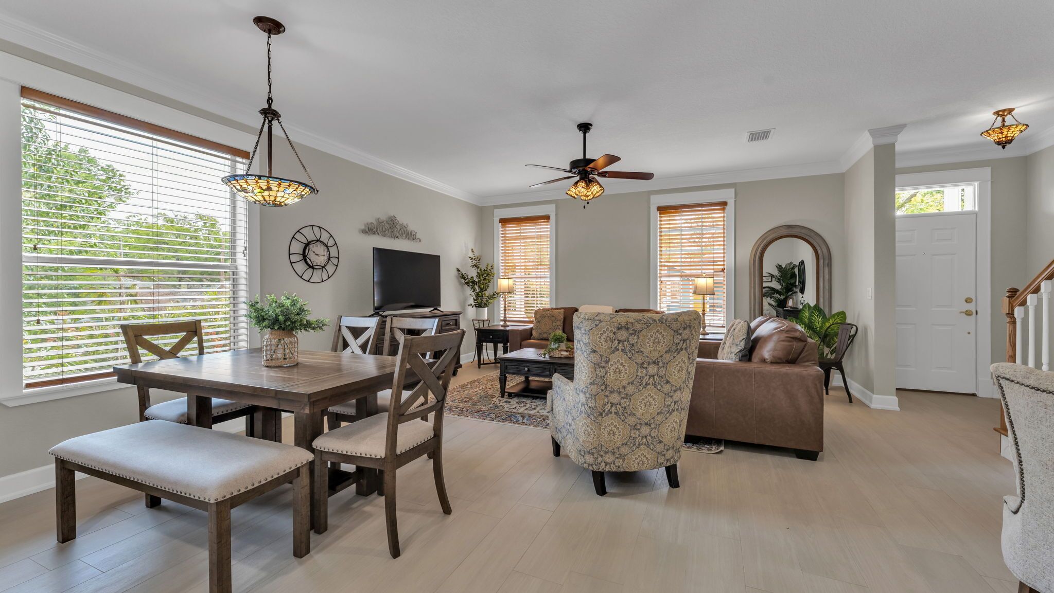 A spacious living room with a dining area, a ceiling fan, and large windows with blinds.