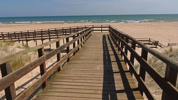 Ein hölzerner Steg führt zu einem Strand mit freiem Blick auf das Meer.