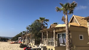 A beachside hotel with wooden structures, palm trees, and lounge chairs.