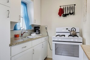 A kitchen with white cabinets, a stove, a coffee maker, and a window with blue curtains.