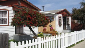 A white house with a red roof, a picket fence, and a tree with red flowers in the front yard. - Charming Cottage: 5-minute walk to beach! (San Diego)