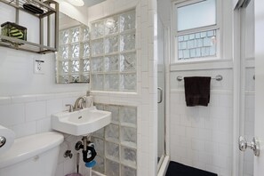 Un baño con un lavamanos blanco, un inodoro, una ducha con puerta de vidrio y un perchero para toallas.