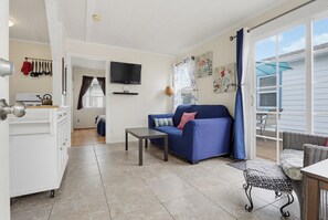 A living room with a blue sofa, a television, and a dining area with wicker furniture.