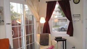 A living room with a sofa, a chair, a small table with a vase, and a window with curtains. - Charming Cottage: 5-minute walk to beach! (San Diego)