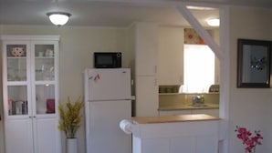 A compact kitchen with a refrigerator, microwave, and a small island. - Charming Cottage: 5-minute walk to beach! (San Diego)
