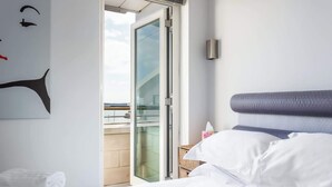 A hotel room with a bed, a glass door leading to a balcony, and a wall-mounted light fixture. - Crow's Nest - Directly on Poole Quay (Poole)