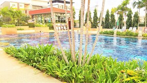 A swimming pool with palm trees and lounge chairs, surrounded by buildings. - Sea View 1-Bed at Jomtien Beach - Sleeps 2 (Pattaya)