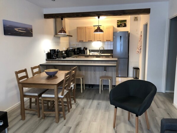 A modern kitchen with wooden cabinets, a stainless steel refrigerator, and a dining area with a wooden table and chairs.