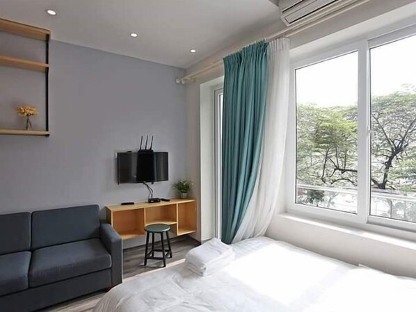 A modern hotel room with a bed, a sofa, a TV mounted on the wall, and a window with curtains.