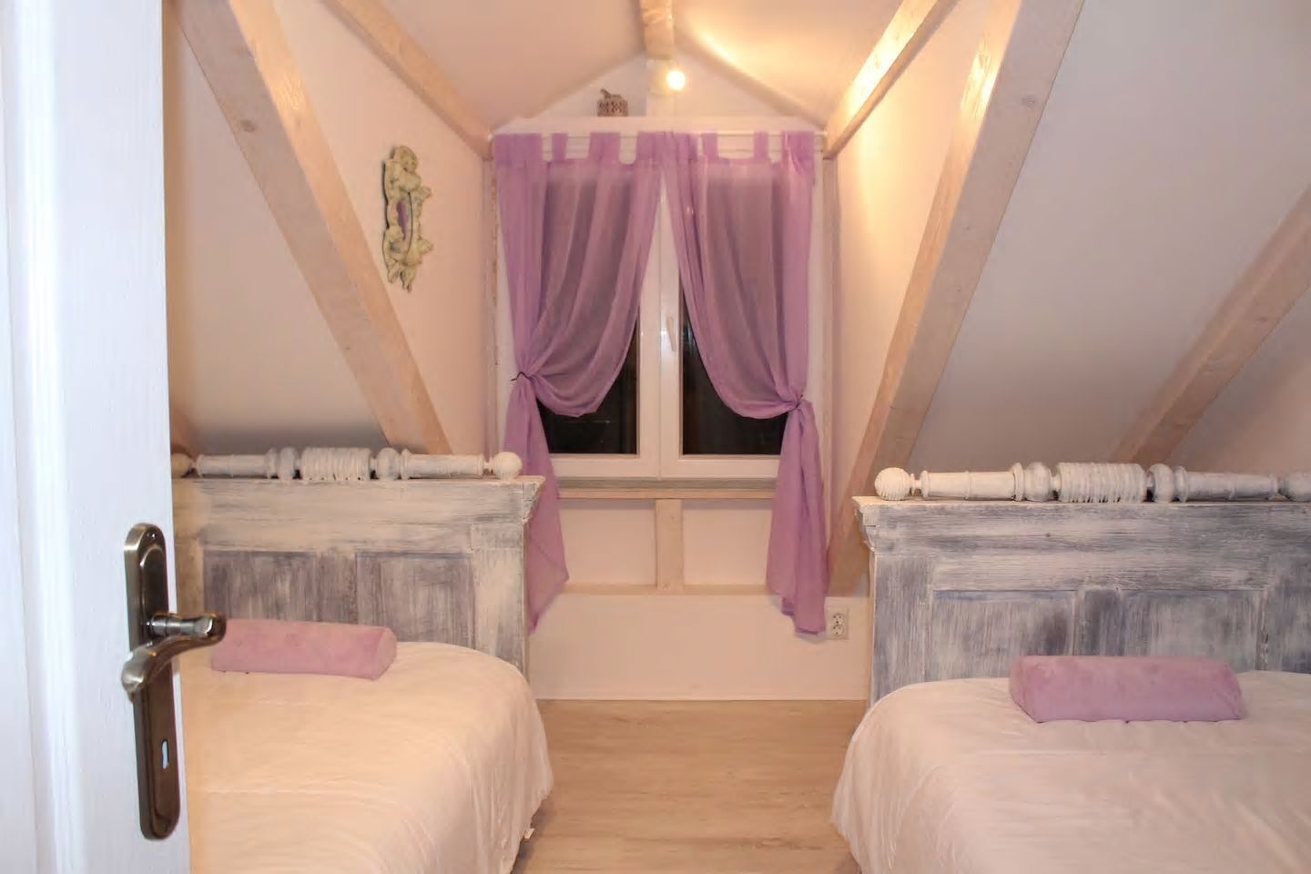 Ein Schlafzimmer mit zwei Betten, einem Fenster mit violetten Vorhängen und einer Holzbalkendecke.