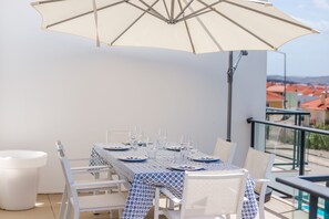 A dining area with a table set for four, white chairs, and a large umbrella providing shade. - Casa Sol & Mar, Stunning Oceanview pool (Lourinhã)