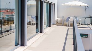 Ein moderner Balkon mit Glastüren, einem Tisch mit Stühlen und einem weißen Sonnenschirm.