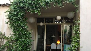 A covered entrance with a glass door, potted plants, a wooden bench, and a table with chairs.