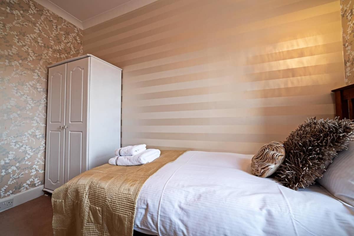 A bedroom with a bed, a wardrobe, and a wall with striped wallpaper.